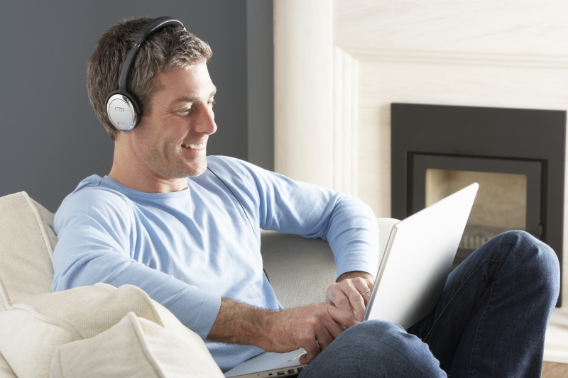 2197575-man-using-laptop-wearing-headphones-relaxing-sitting-on-sofa-at-home